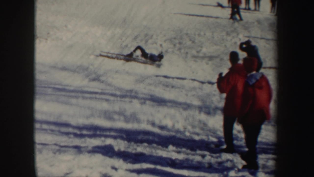 Skier fallen on snow while red-coated spectators stand nearby.