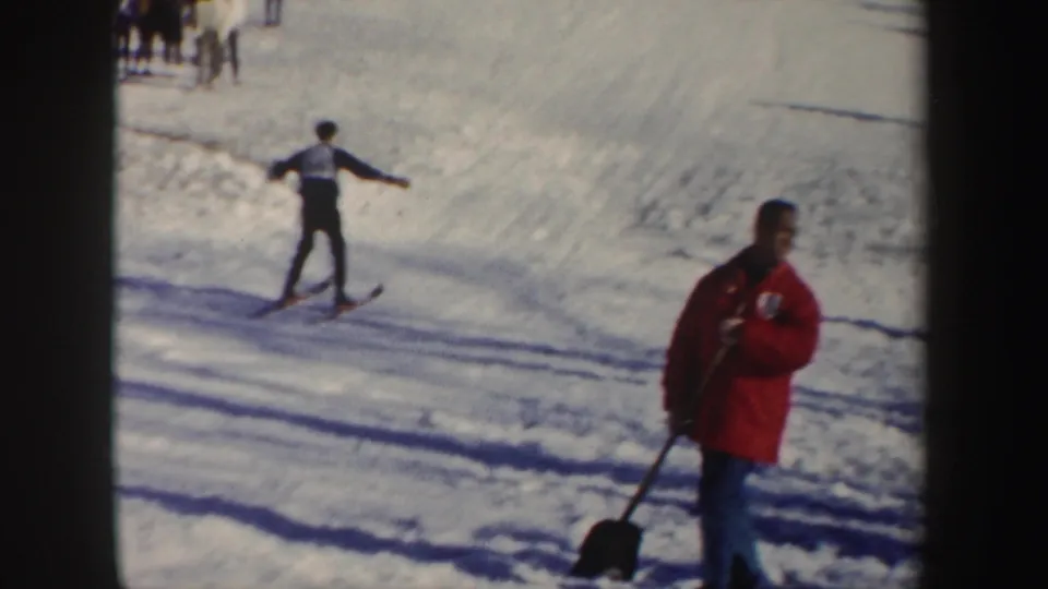 1962 New York ski-slope frame with a skier on the course and a red-jacketed person standing with a shovel.