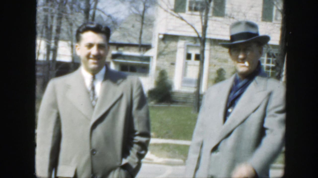 Two adult men remain facing the camera outside a Massachusetts house in 1949, with the older man in a fedora and the younger man in a tie.