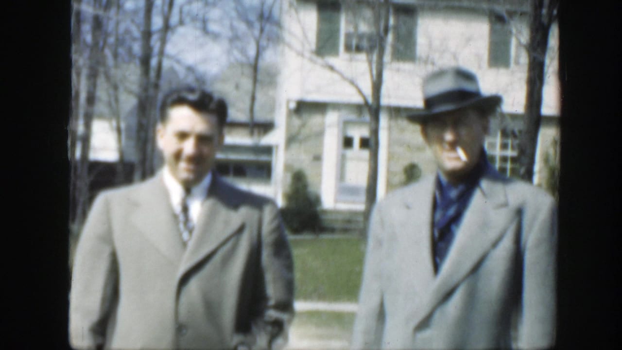 In this 1949 Massachusetts frame, two men in gray outerwear stand outdoors; the fedora-wearing man appears to hold a cigarette.