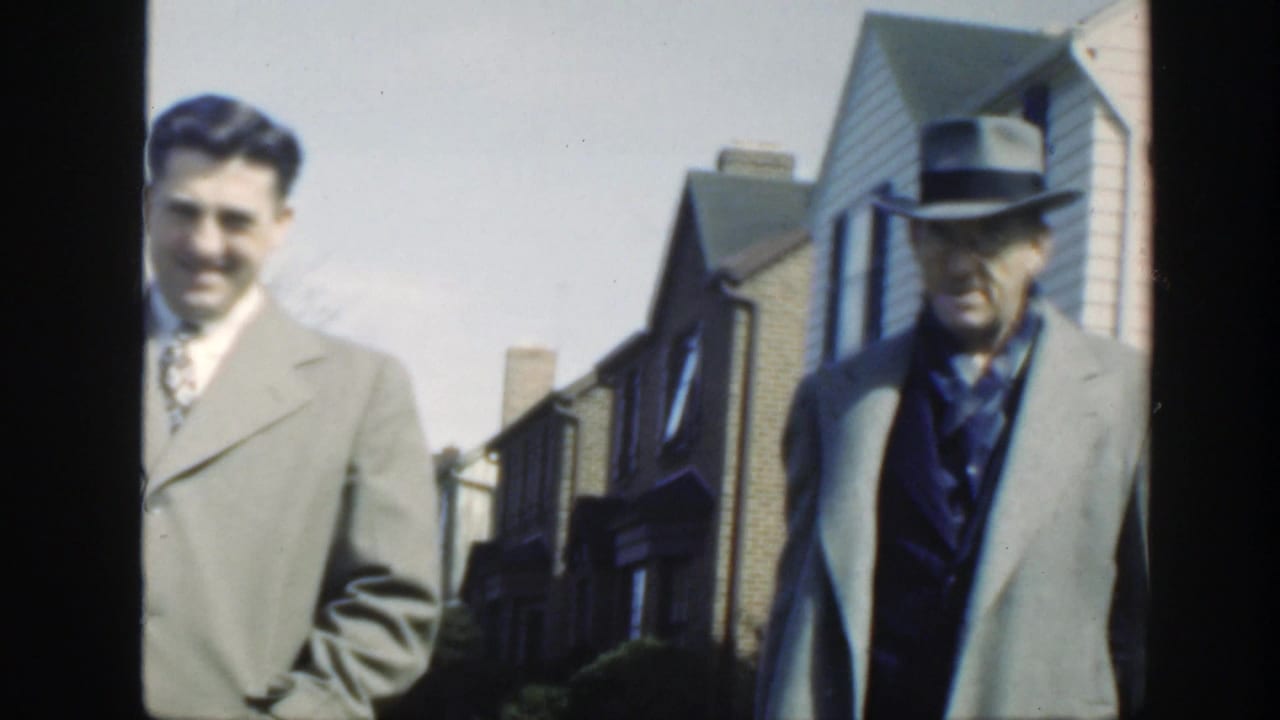 Two men in suits stand or walk near houses, one smiling toward the camera.