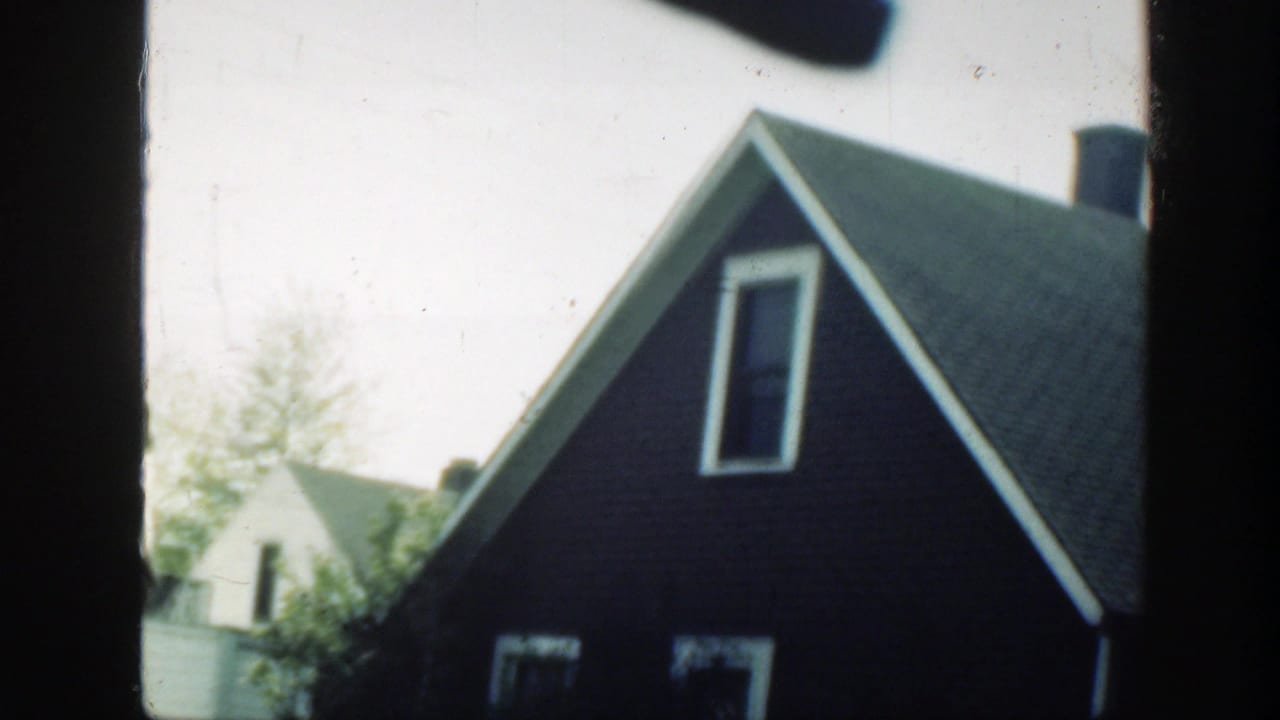 1949 Massachusetts home-movie frame showing a dark-sided residential house with a steep roof and nearby neighboring homes.