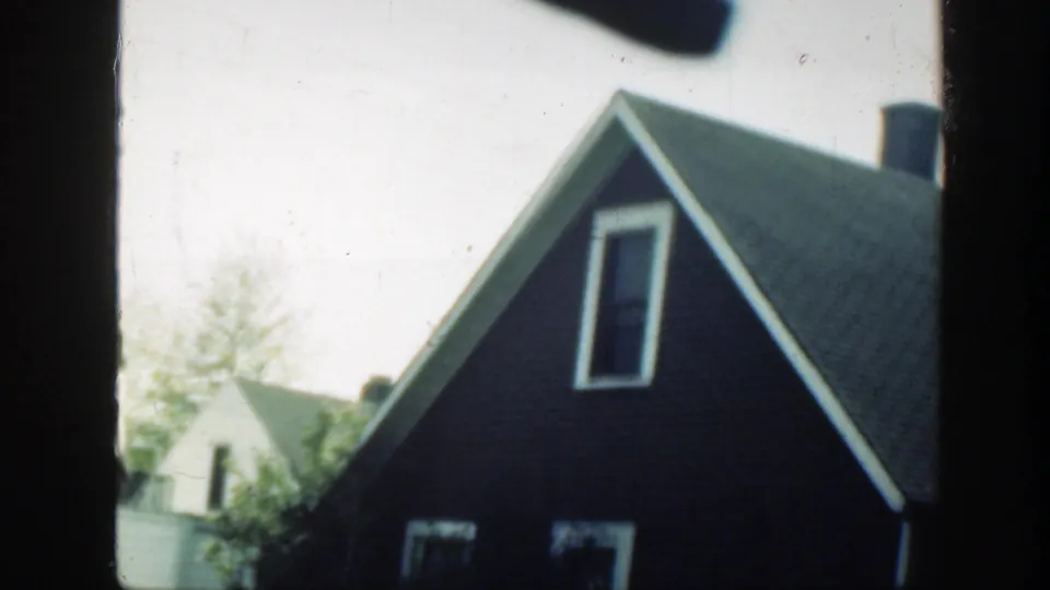 1949 Massachusetts home-movie frame showing a dark-sided residential house with a steep roof and nearby neighboring homes.