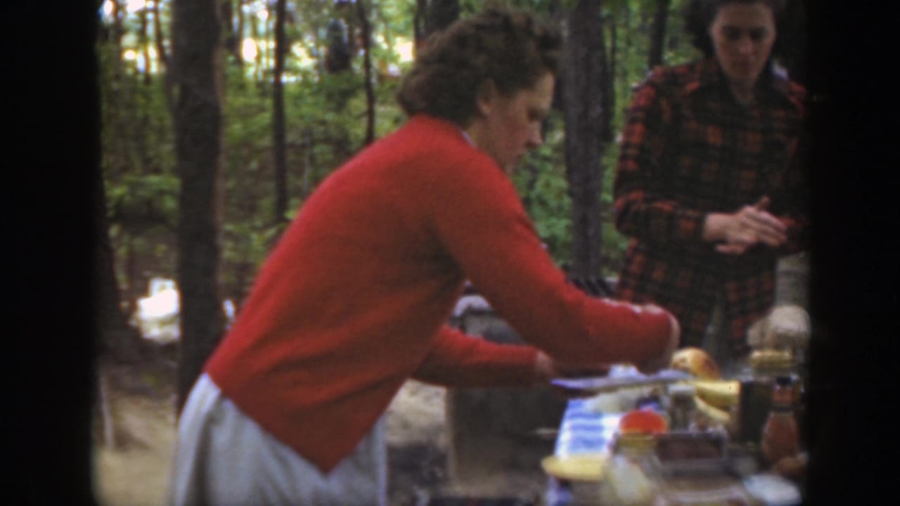 1949 Massachusetts picnic scene with a woman in a red cardigan serving at a table and another woman standing in a plaid jacket.