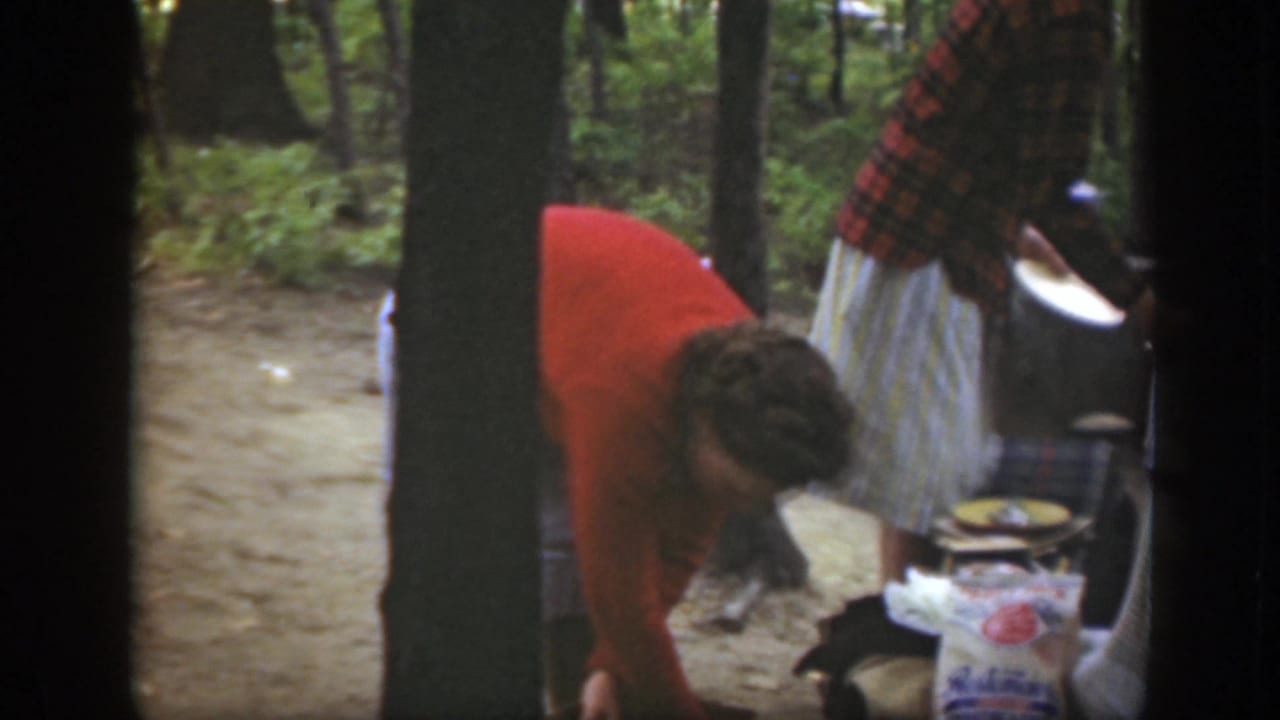 1949 Massachusetts frame showing campsite preparation, with one woman bending over supplies and another holding a plate.