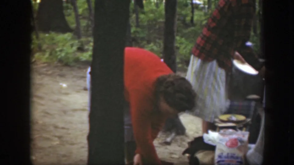 1949 Massachusetts frame showing campsite preparation, with one woman bending over supplies and another holding a plate.