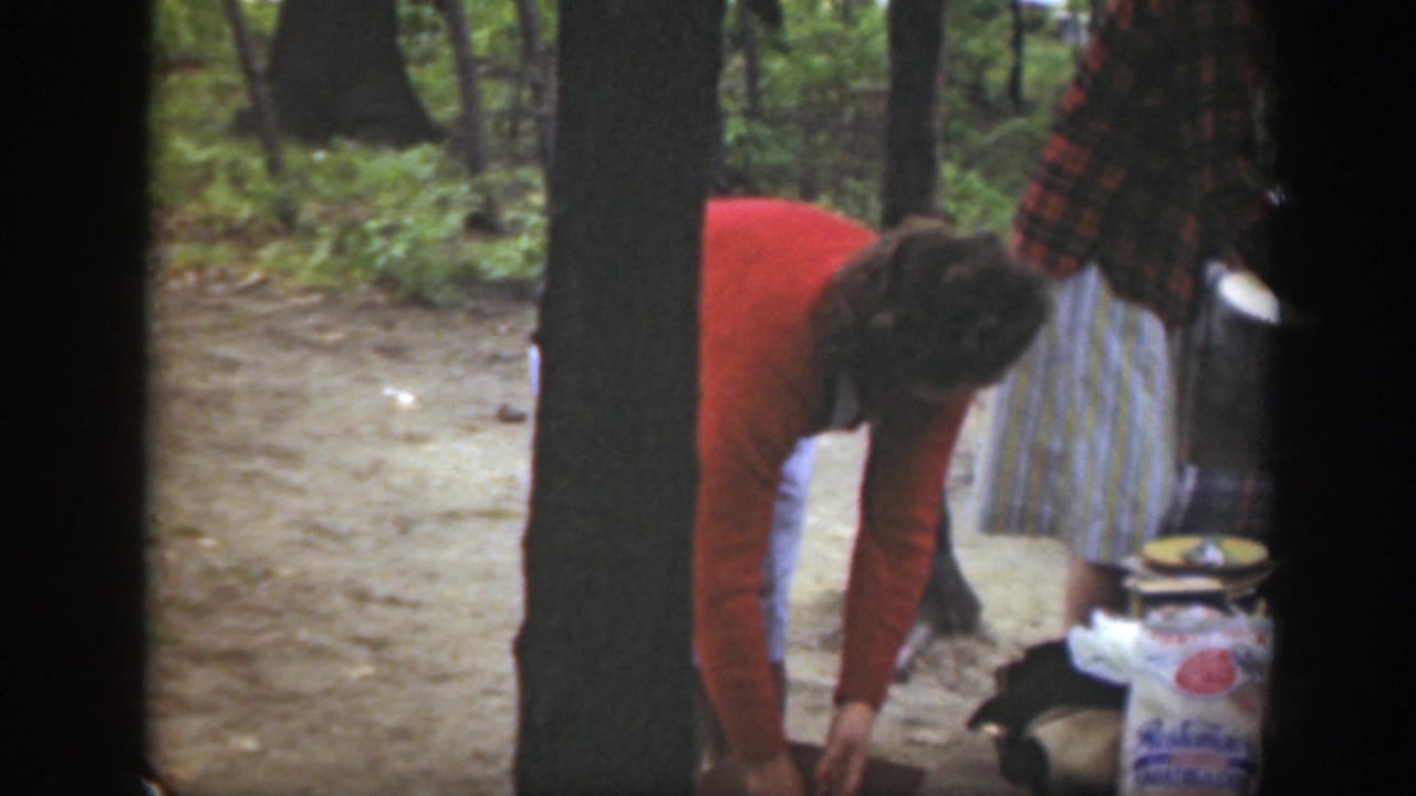 1949 Massachusetts home-movie frame of a woman reaching down by boxed campsite supplies while another woman stands nearby.