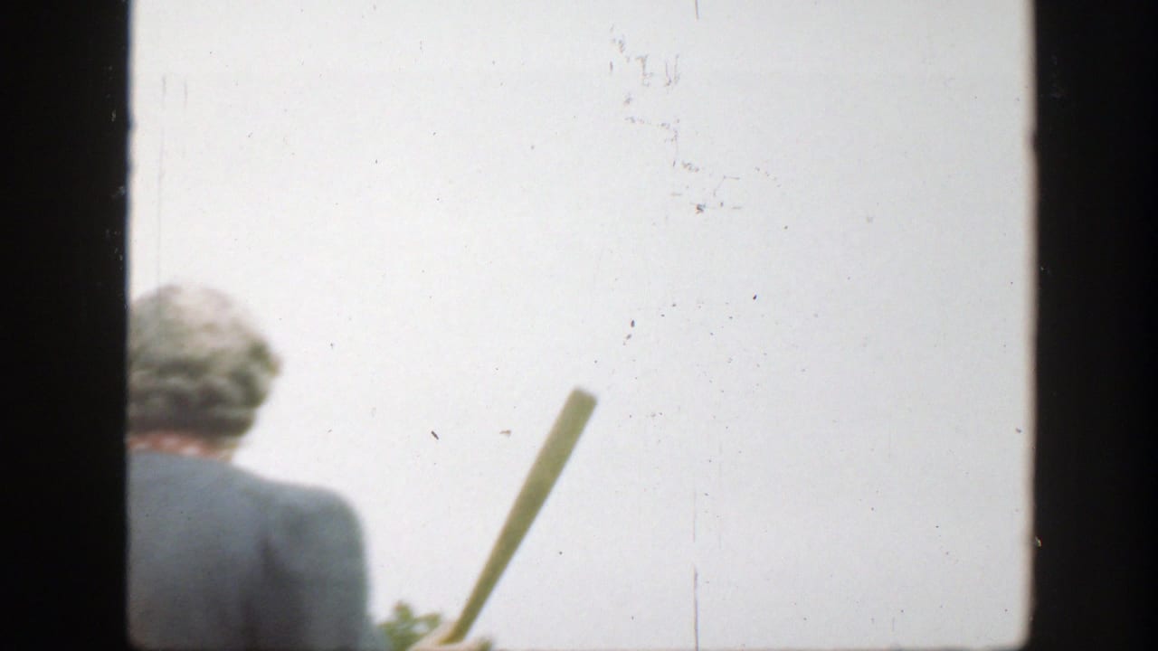 The woman turns away while holding a wooden baseball bat, with trees low in the frame and bright sky behind her.