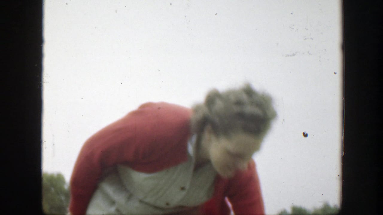 The woman bends forward near the lens, partly filling the frame, in soft 8mm footage from the outdoor Massachusetts scene.