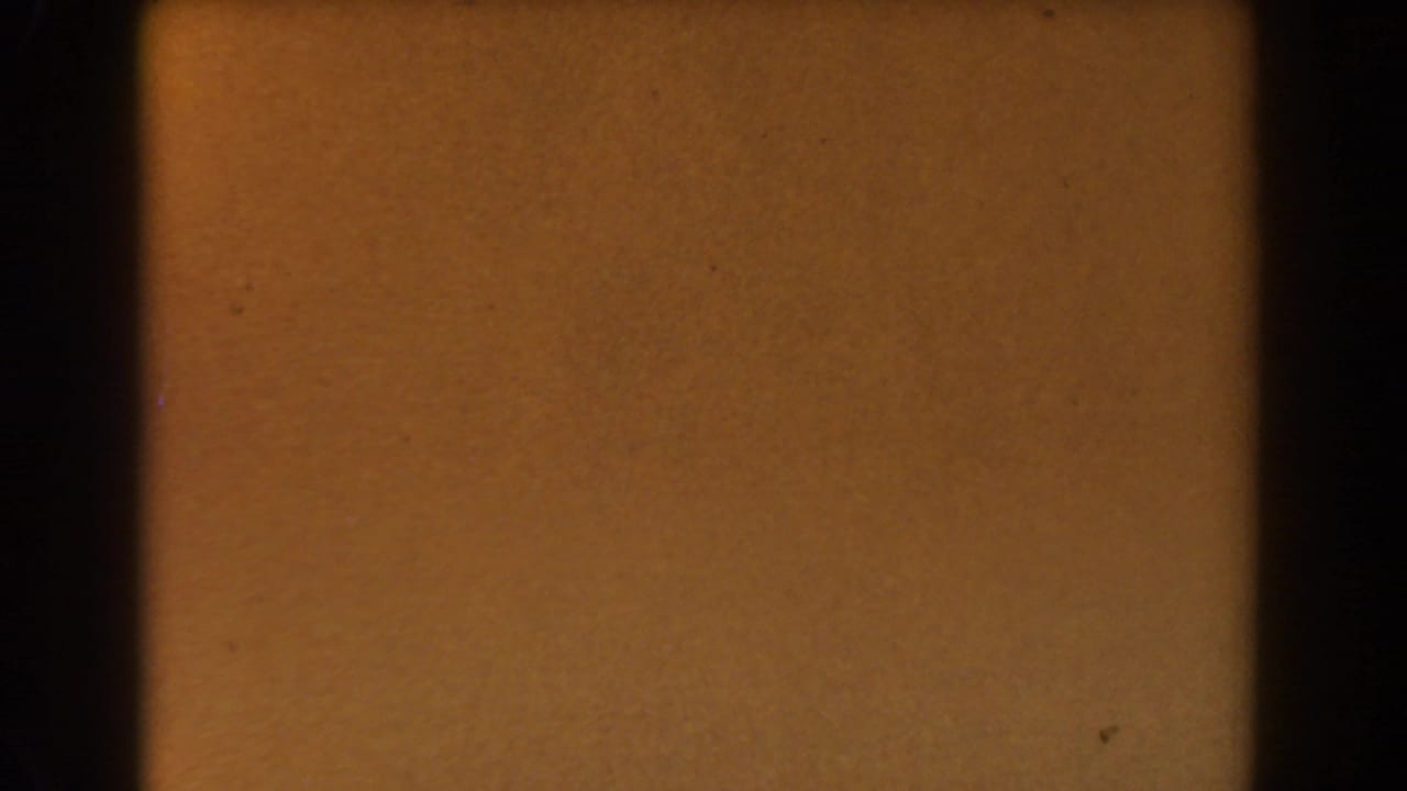 Amber-toned 8mm frame from the 1962 Glendale clip, with dark borders, grain, and small specks visible.