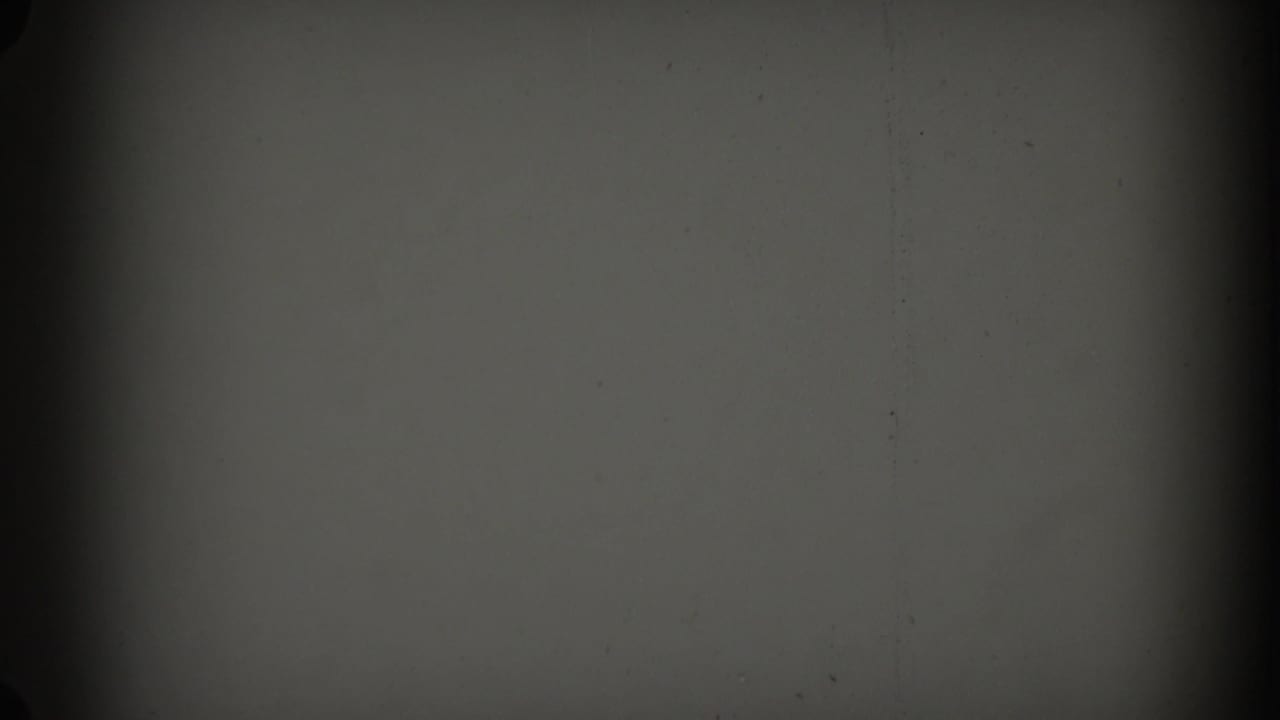 Gray film frame with grain, small specks, and a dark vertical band near the left edge.
