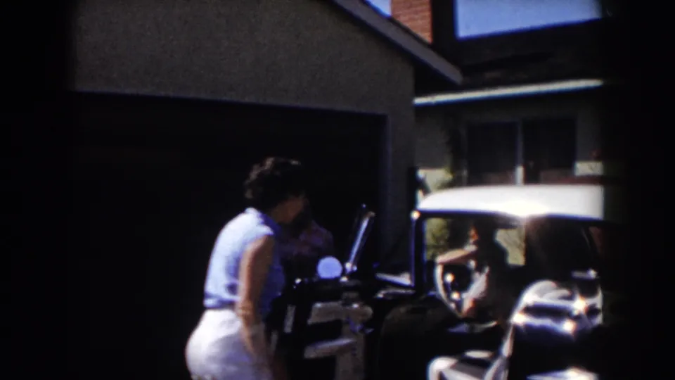 A woman stands by the open white car while another adult appears in the garage shadows in the Glendale driveway scene.