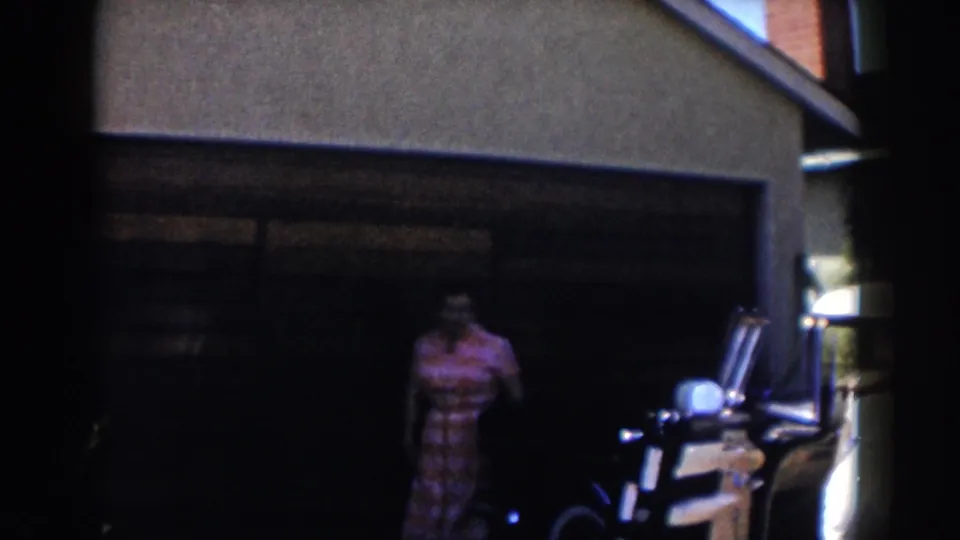 The person in a pink patterned dress appears in the shaded garage entrance beside the white car in the 1962 Glendale footage.