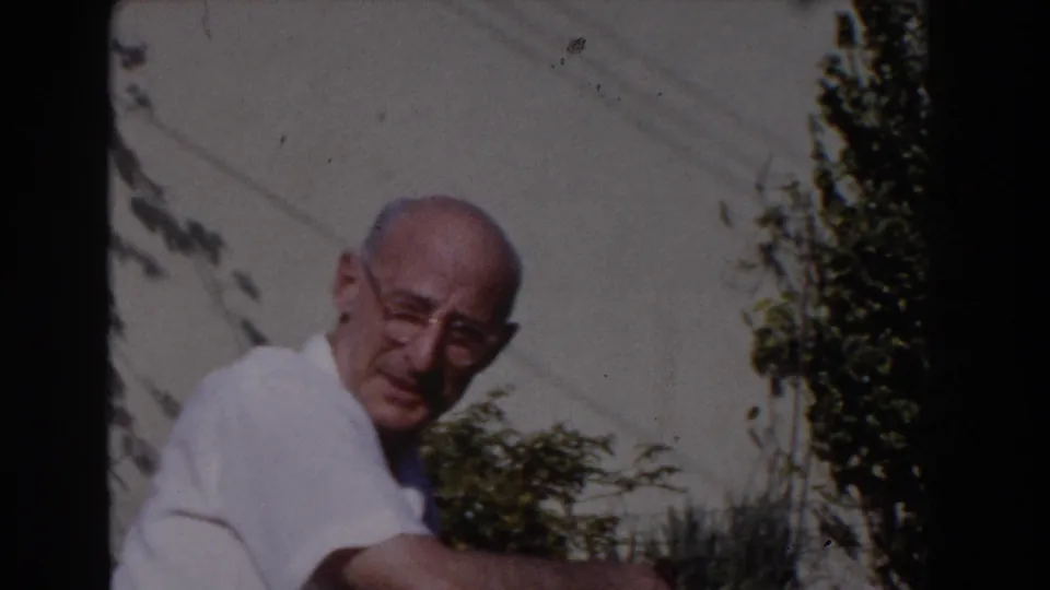 The older man in glasses looks toward the camera or game area, framed against shrubs and a pale backyard wall in Glendale.
