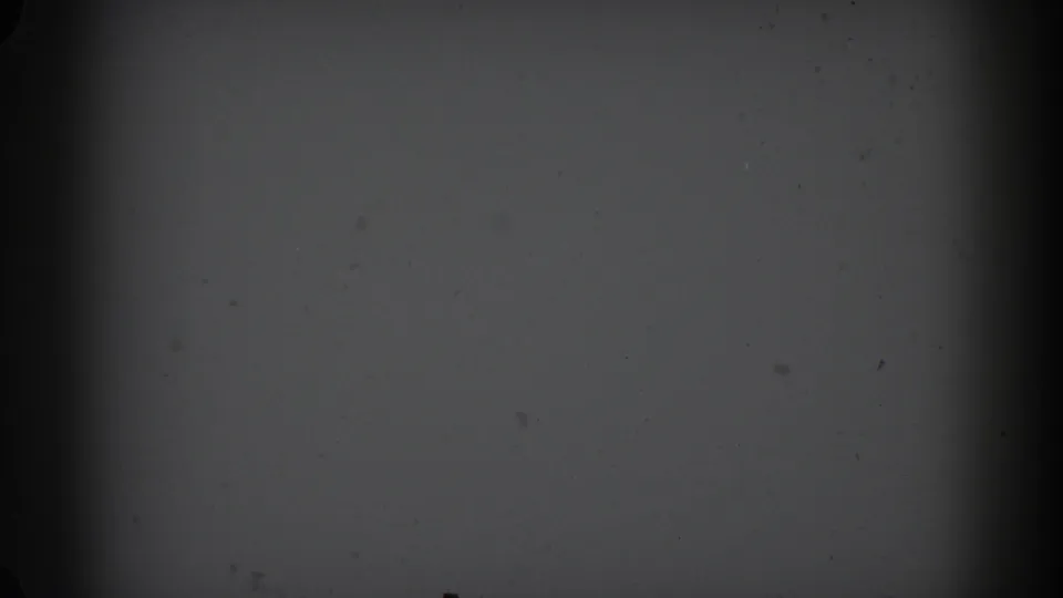 1962 Glendale 8mm frame showing a pale paper-like surface under low light, with dust specks, soft focus, and dark edge falloff.