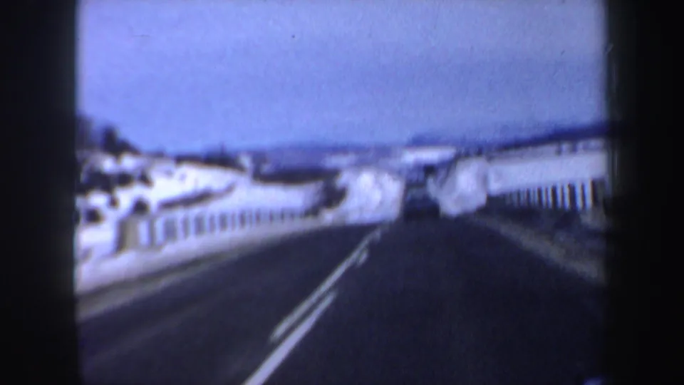 1962 New Hampshire driving frame showing a snowy roadside, white railings, double center lines, and distant winter hills.