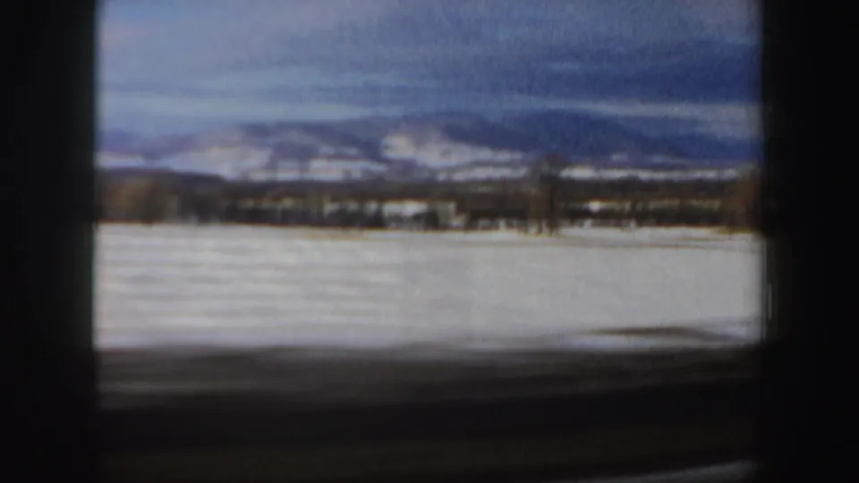 A New Hampshire winter field fills the frame, with distant hills, low tree lines, and cloudy sky in soft 8mm texture.