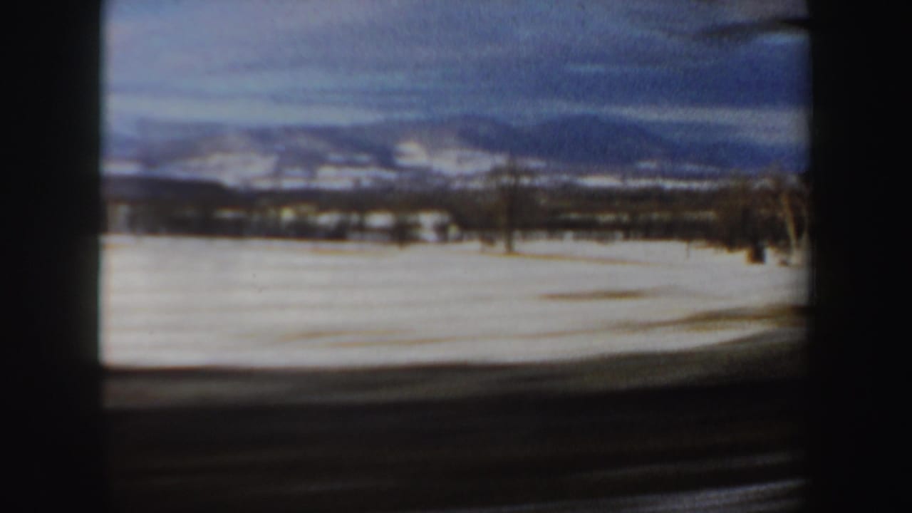 1962 New Hampshire home-movie view of a snowy field, distant mountains, cloudy sky, and dark car-window framing.