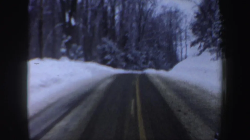 New Hampshire 1962 car POV along a narrow plowed road, with a yellow center line, heavy snowbanks, and winter forest on both sides.