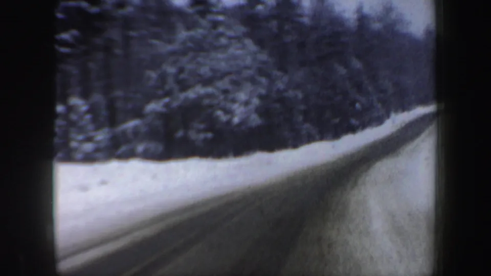 Home-movie frame from New Hampshire showing forward travel past snowy evergreens and a plowed rural road.