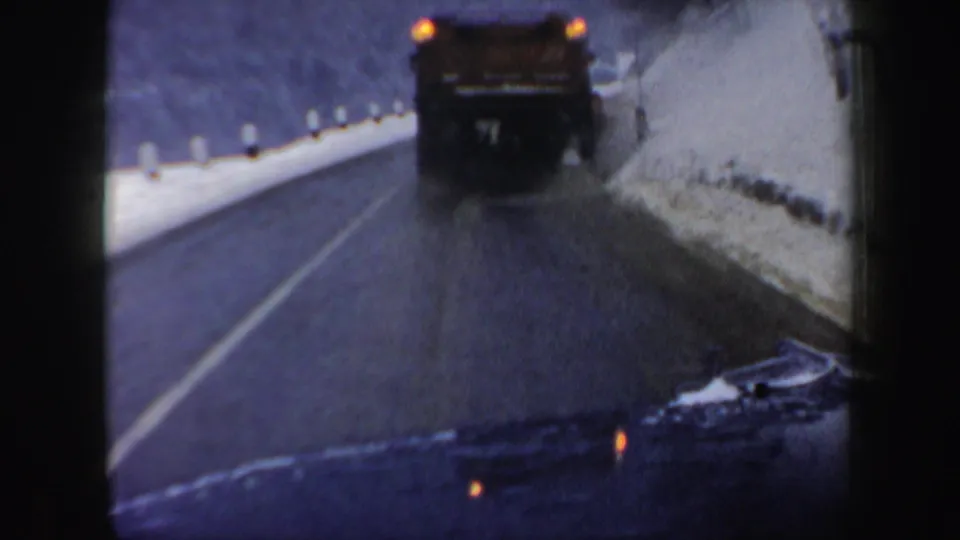 1962 New Hampshire winter road frame showing a plow moving close to the snowbank as the camera follows from behind.