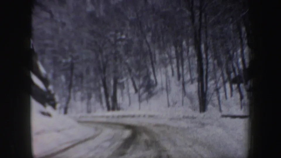 1962 New Hampshire home-movie frame showing a snowy forest road curving ahead from a vehicle interior viewpoint.
