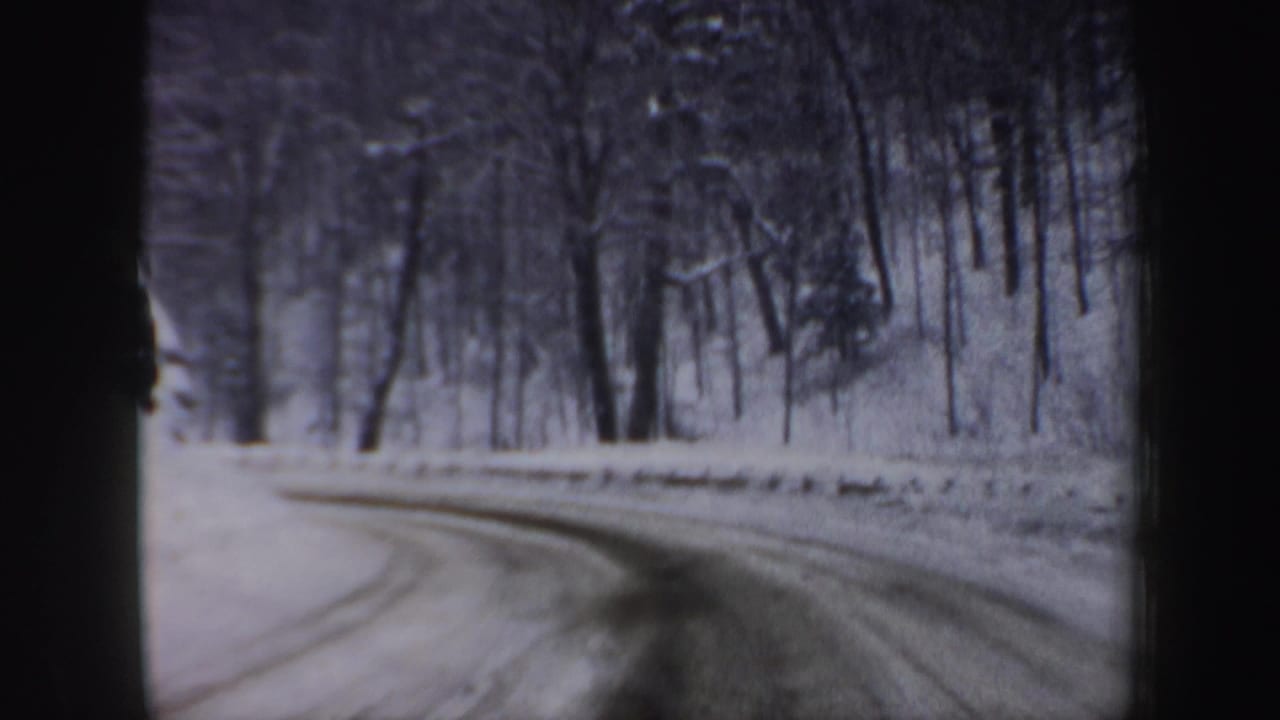 Snowy road bends right through woodland, bordered by high snow and bare trees.