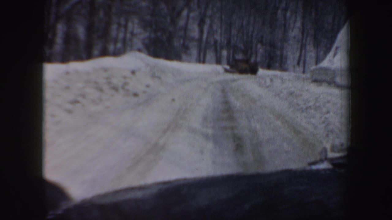1962 New Hampshire 8mm frame showing a snowy winding road from inside a moving car, with bare trees and dashboard visible.