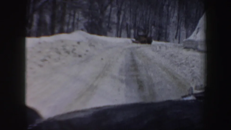 1962 New Hampshire 8mm frame showing a snowy winding road from inside a moving car, with bare trees and dashboard visible.