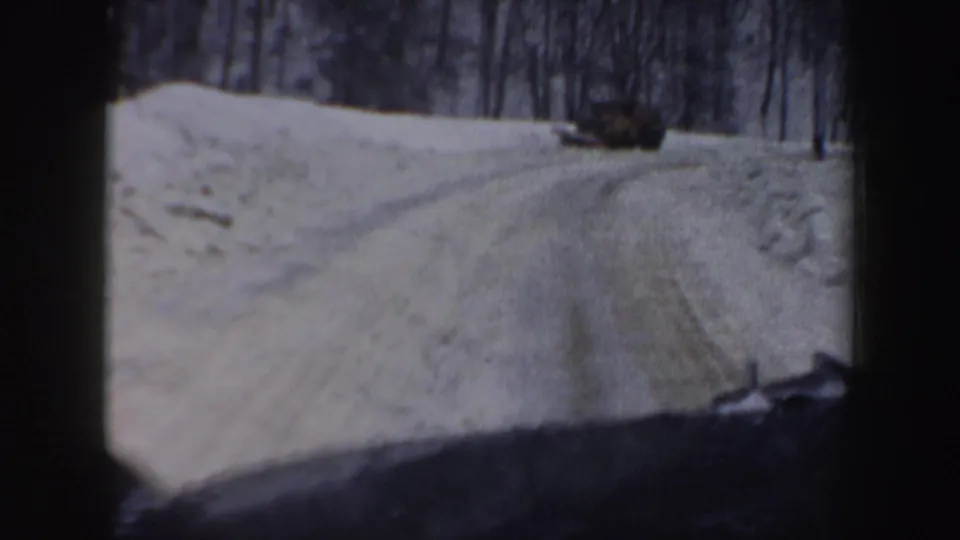 In-car 8mm view of a winding snow-covered New Hampshire road in 1962, framed by dashboard shadow and winter trees.