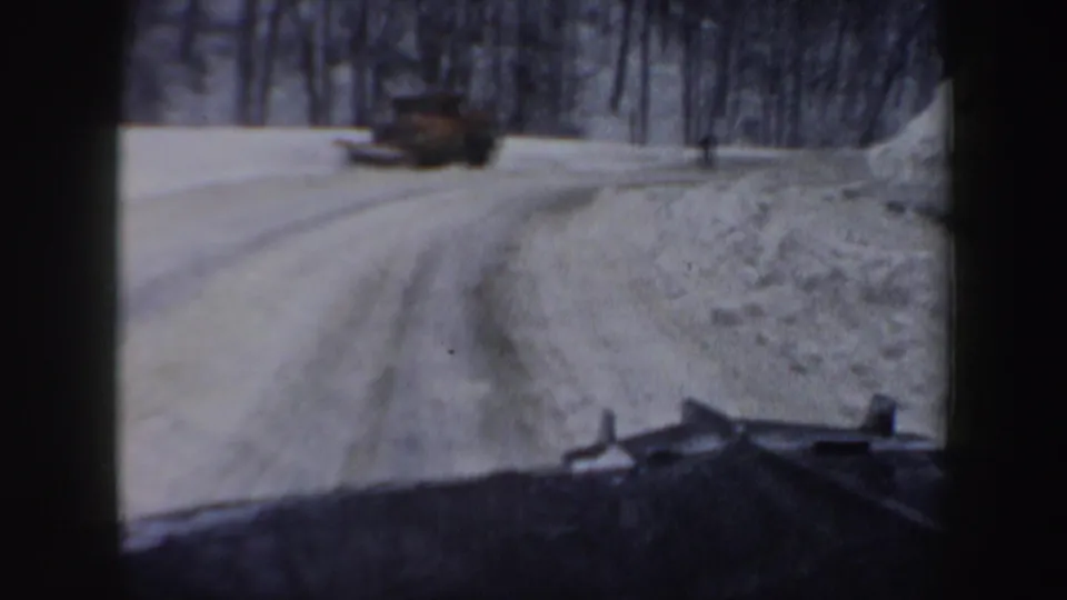 1962 New Hampshire home-movie frame of a car traveling past snowbanks on a wooded winter road.
