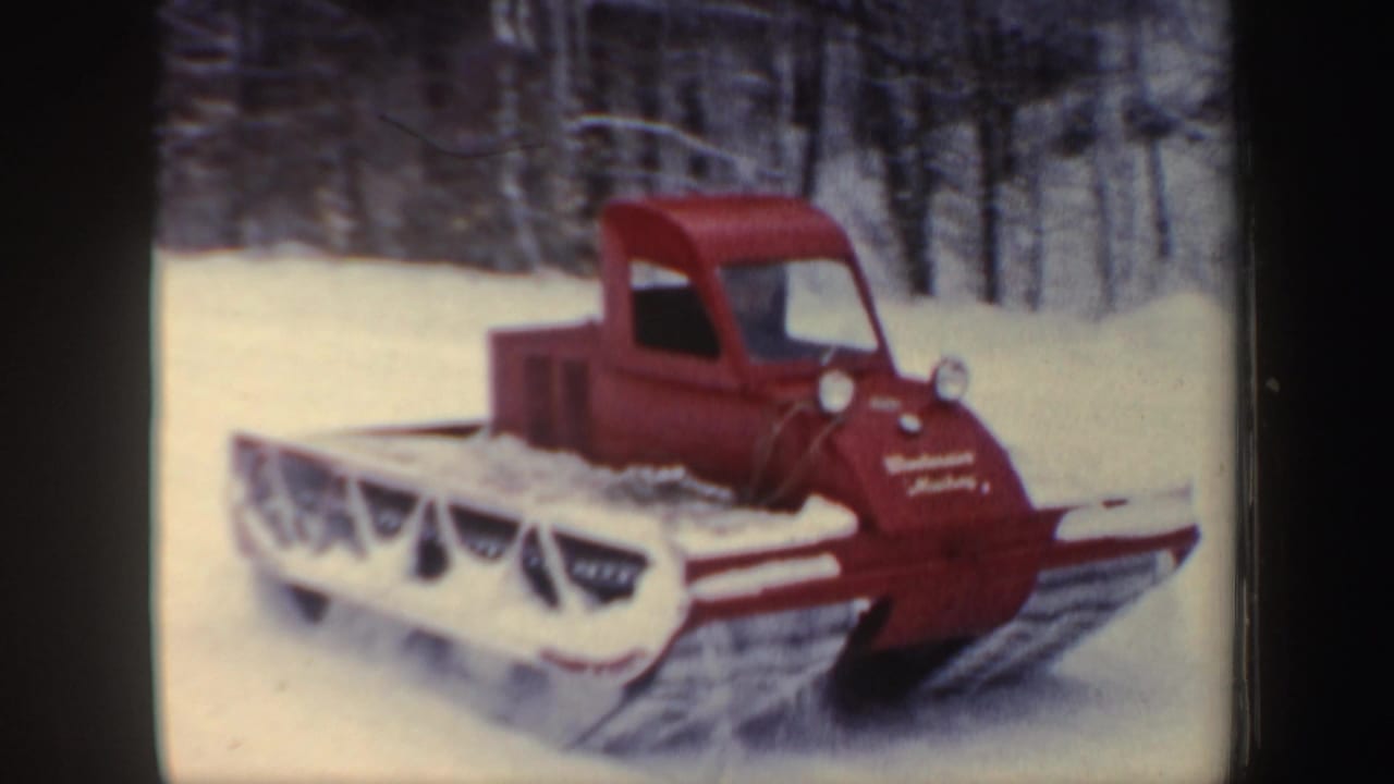 Red snowmobile parked or moving through snow with winter trees behind it.