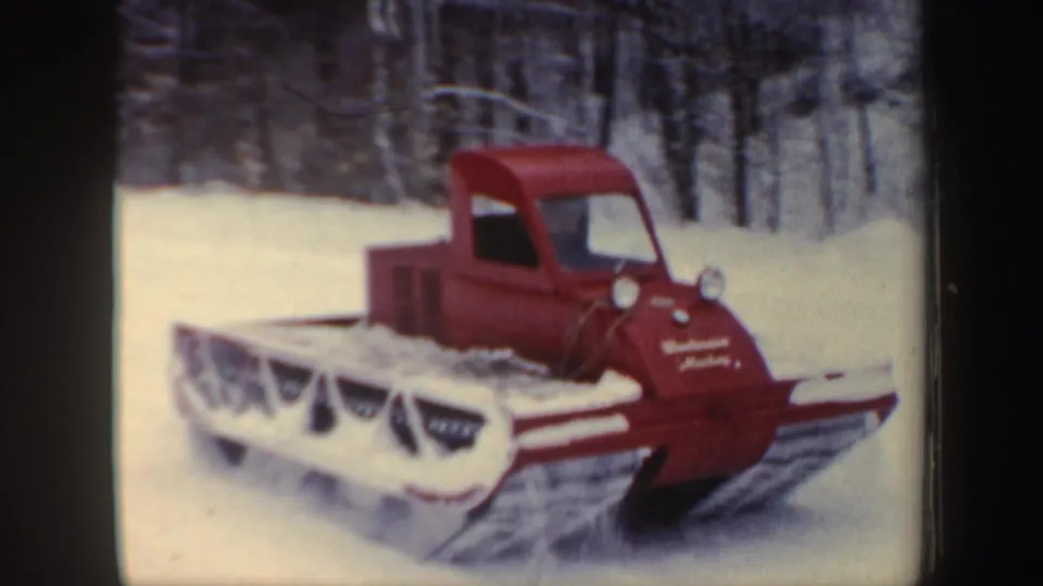 Red snowmobile in snowy New Hampshire woods, seen in 1962 8mm home-movie footage with front ski and track visible.