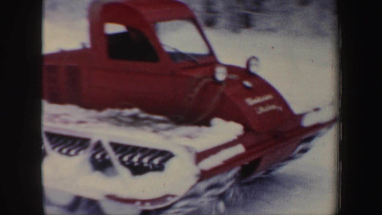 Closer view of a red snowmobile nose and track in snowy woods.