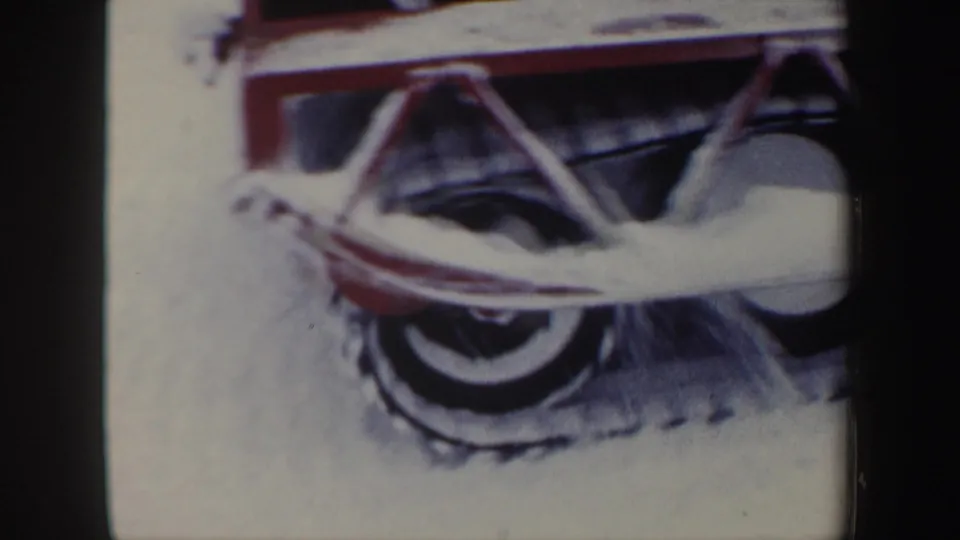 Detailed 8mm frame of the red snowmobile's rear track area and wheel assembly moving through snow.