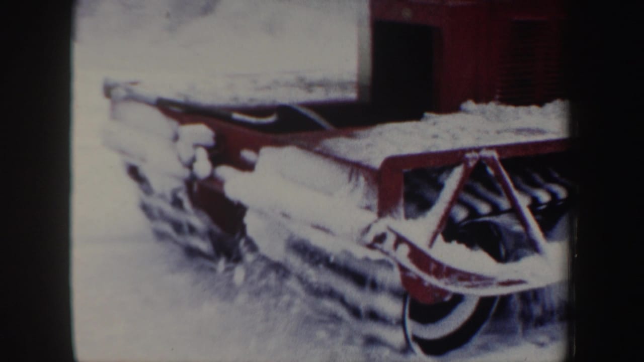 Red tracked snow vehicle close to the camera with snow piled on its treads.
