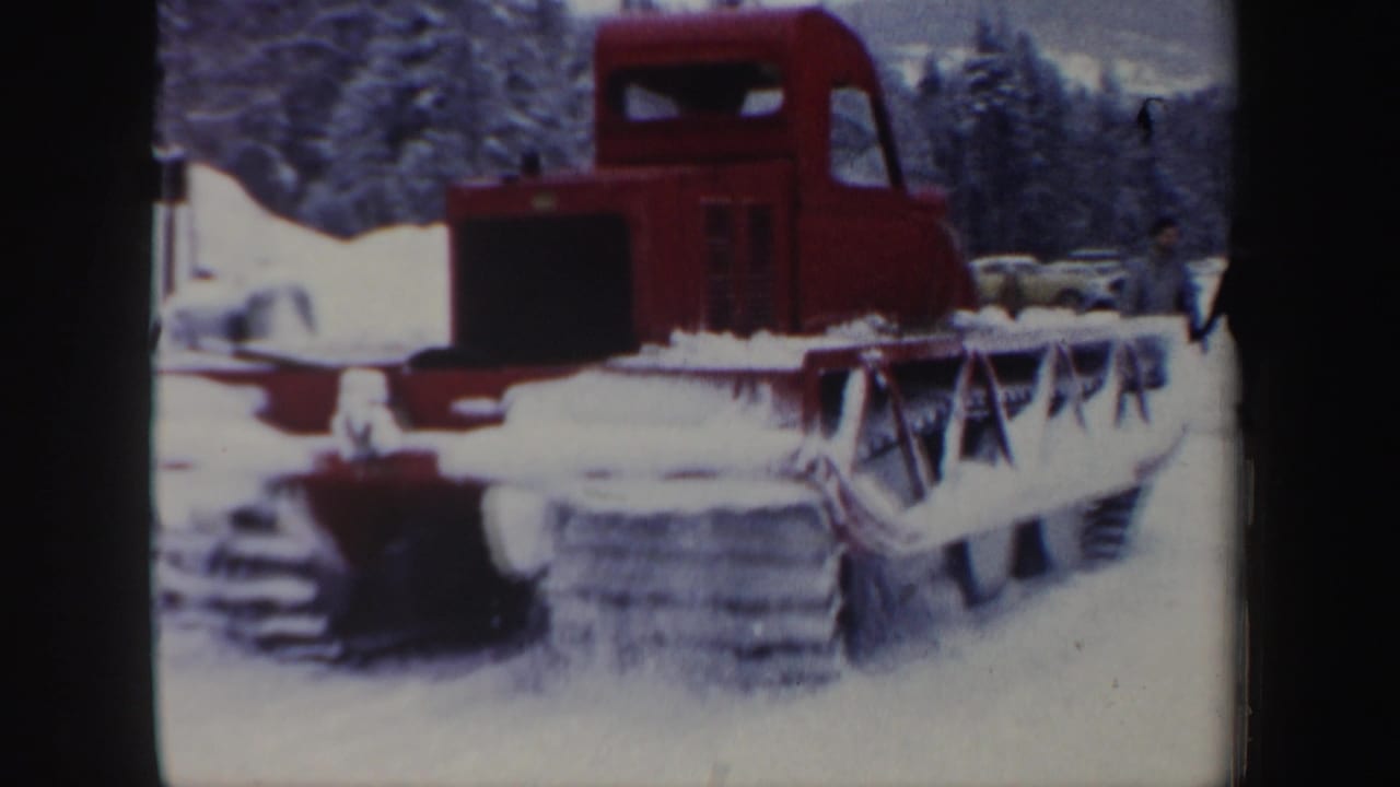 Red tracked snowplow facing forward in a snowy wooded area.