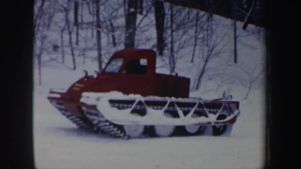 1962 New Hampshire 8mm frame showing the side of a red tracked snow vehicle with its wide treads and front framework visible in deep snow.