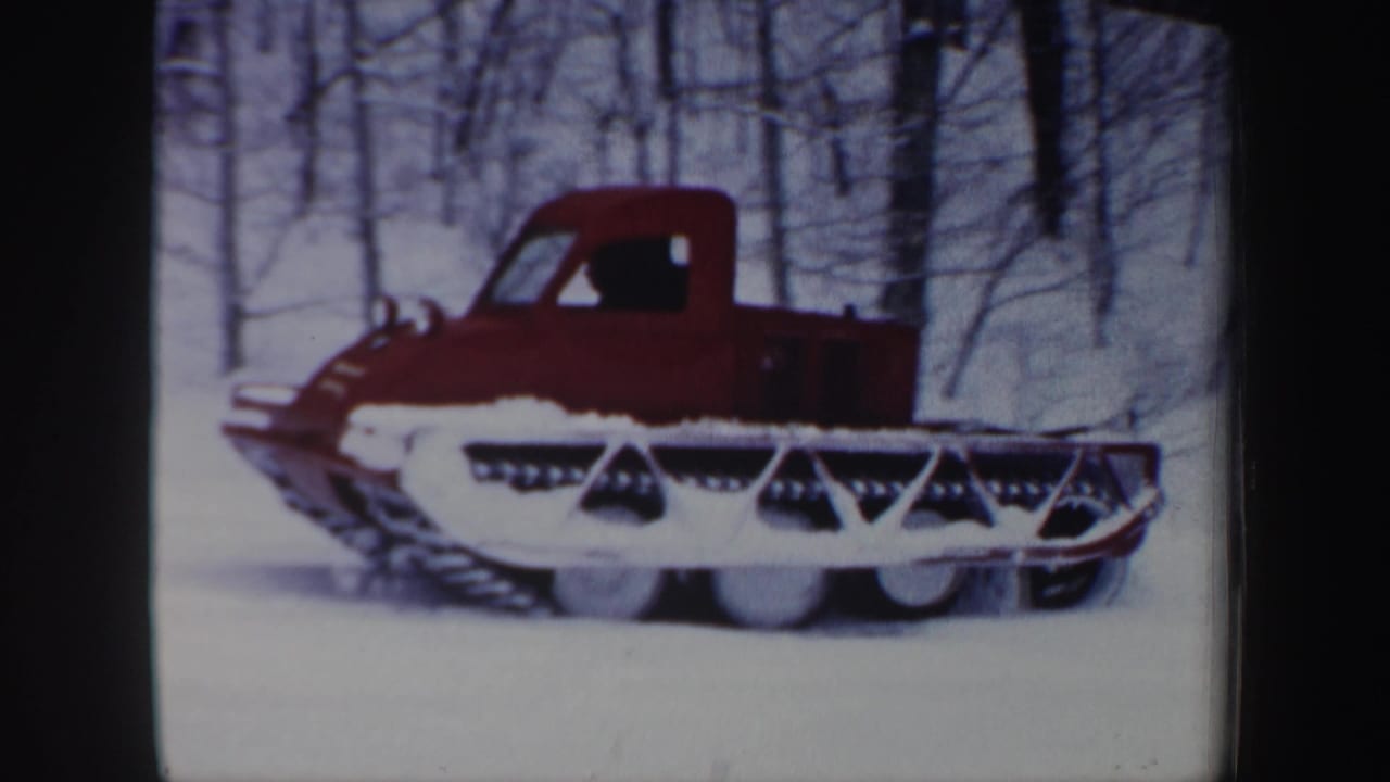 Red tracked utility vehicle moves across snowy New Hampshire woods in 1962 home-movie footage.