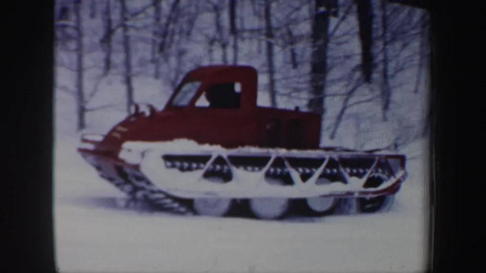 Red tracked utility vehicle moves across snowy New Hampshire woods in 1962 home-movie footage.