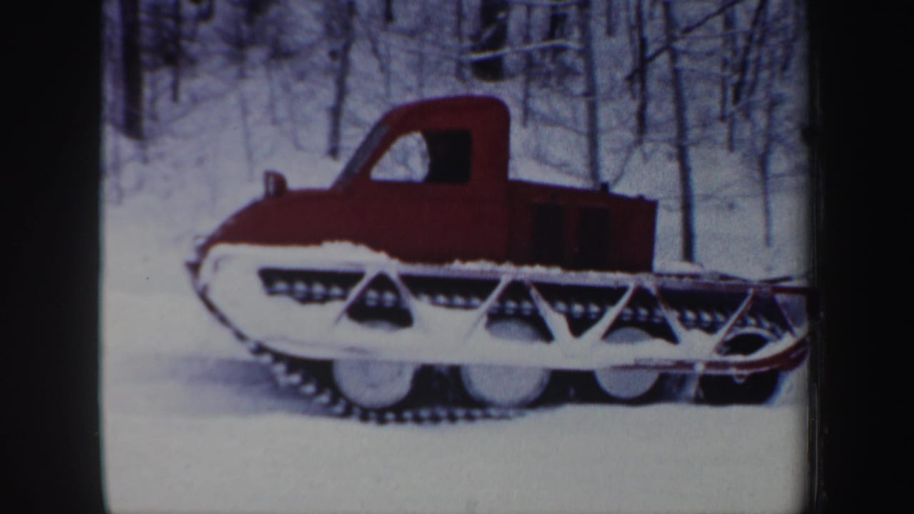 Red tracked vehicle on snow with winter woods behind it.