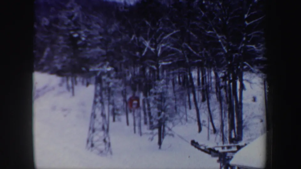 Snow-covered woods and ski-lift hardware frame a distant red tracked vehicle in 1962 New Hampshire footage.