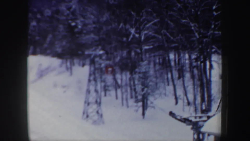 A distant red tracked vehicle is seen through snowy woods near ski-lift equipment in New Hampshire, 1962.