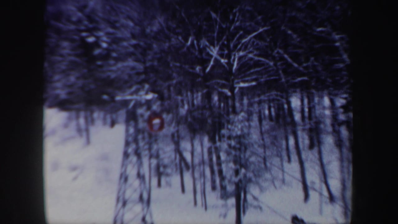 1962 New Hampshire 8mm frame showing snowy trees and a small red cable car partly visible in the winter landscape.