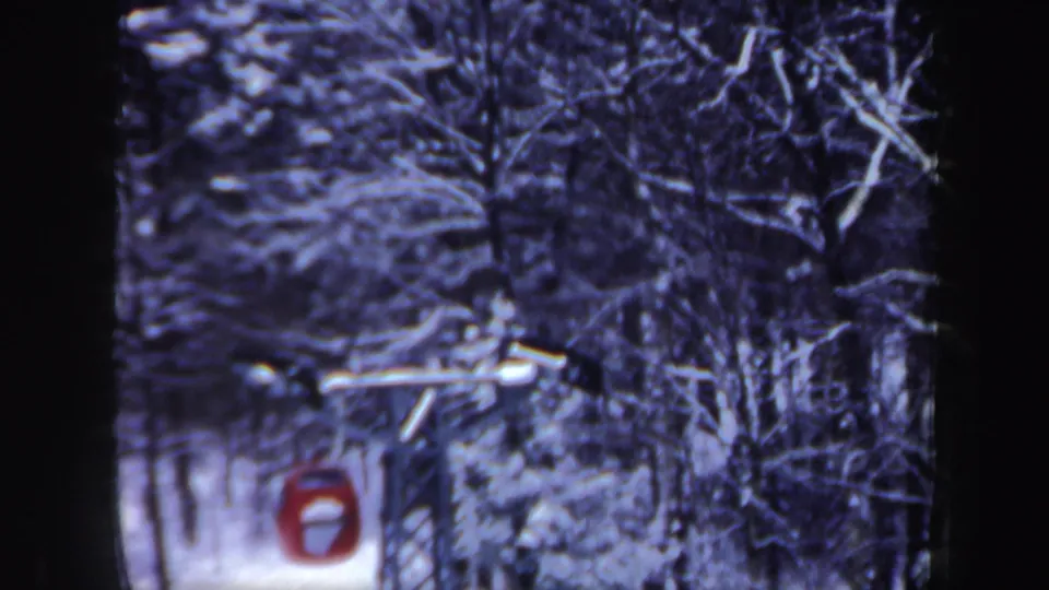 1962 New Hampshire 8mm frame showing the red cable car closer to camera, framed by dark trunks and snowy branches.