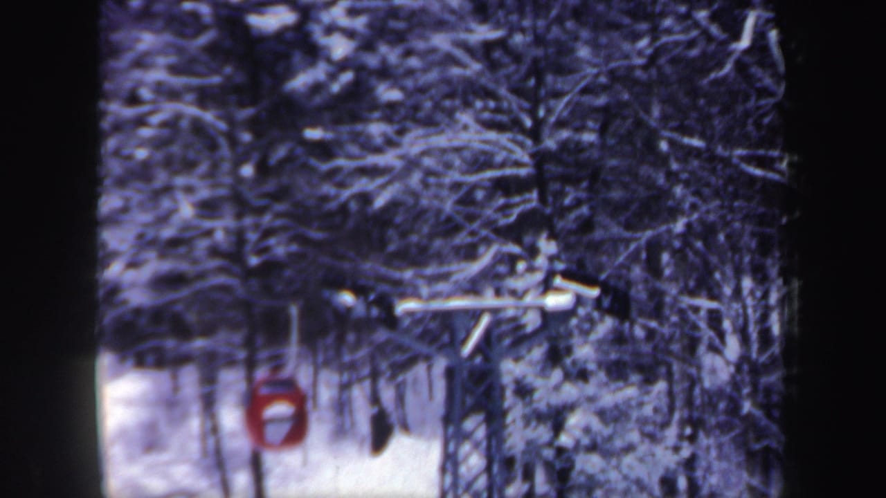 Red gondola bucket on a ski lift among snow-covered trees.