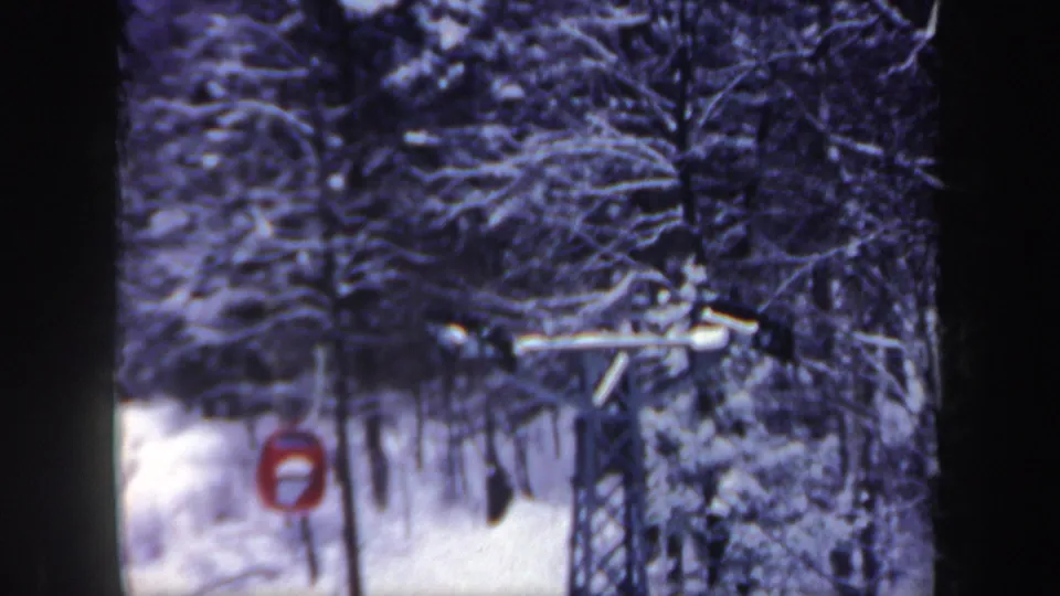 1962 New Hampshire frame with a red bucket lift car, overhead cable, support tower, and dense snow-covered woods.