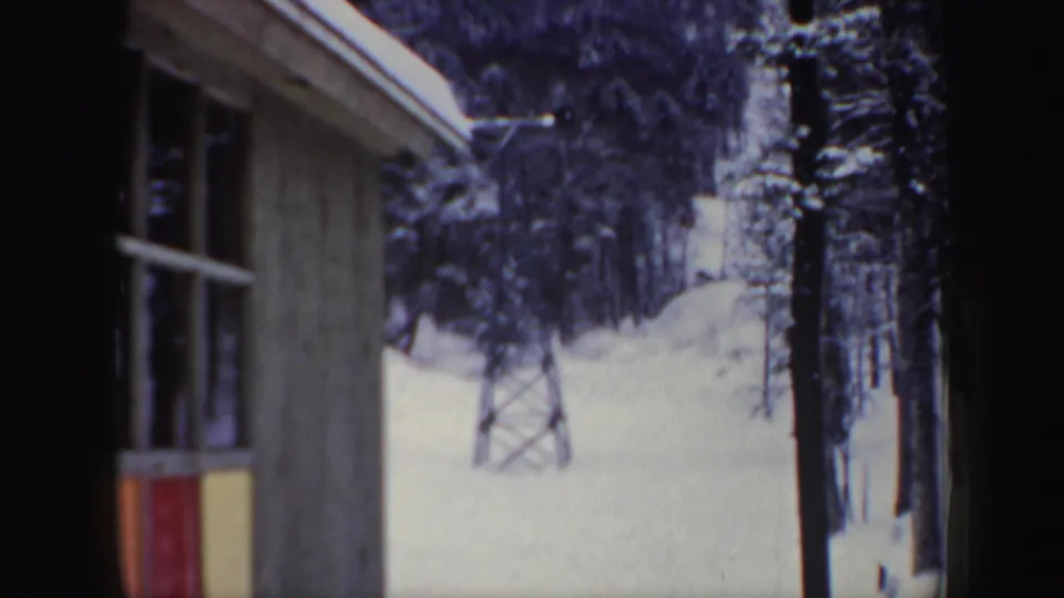 1962 New Hampshire ski-area view with a wooden building in the foreground and a lift tower beyond the snow.