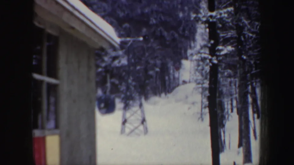 The frame shows a New Hampshire winter ski-area scene with a building edge, snowy slope, trees, and a lift tower.