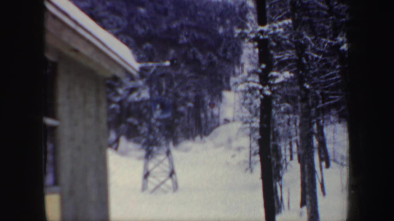 1962 New Hampshire home-movie frame showing snow-covered trees, a tan building edge, and a distant ski lift tower.